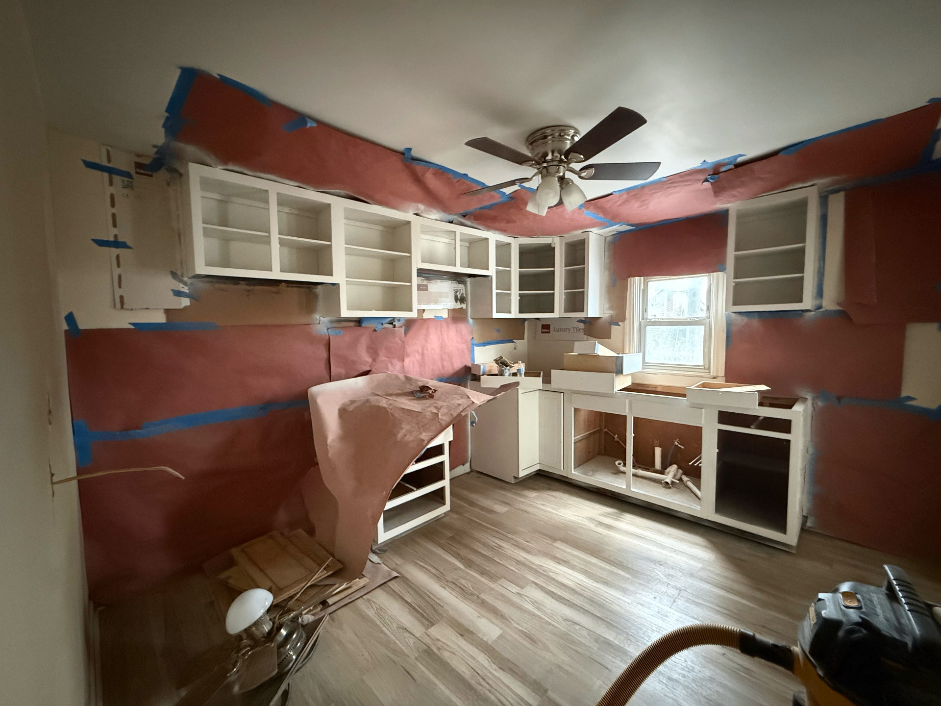 Full kitchen remodel mid-project — cabinets painted white, walls fully masked with rosin paper for spray prep