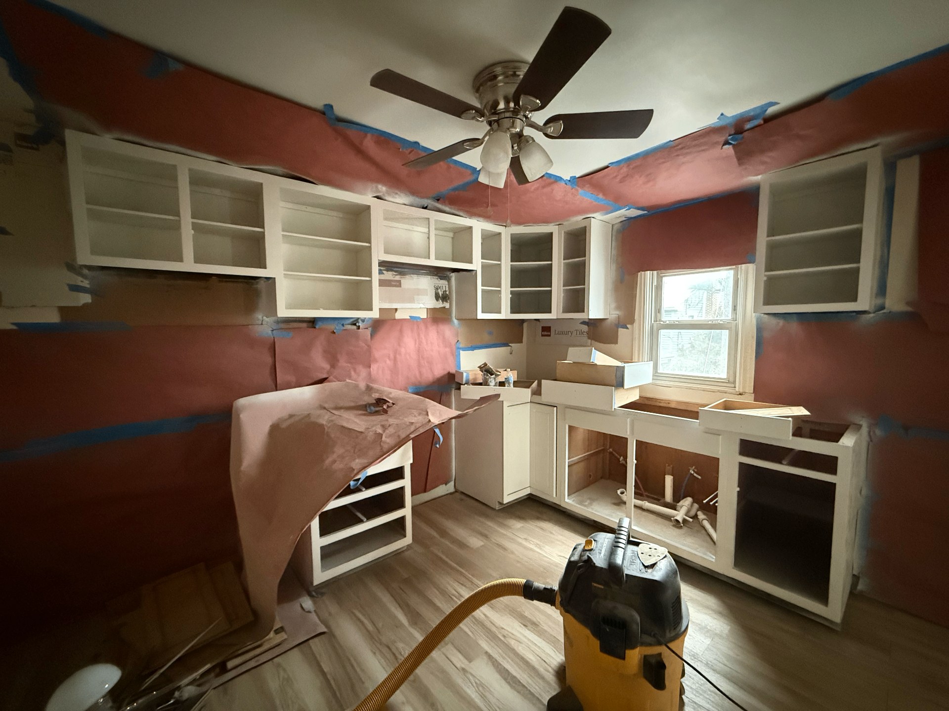 Kitchen remodel in progress — cabinets masked with rosin paper and tape, prepped for paint