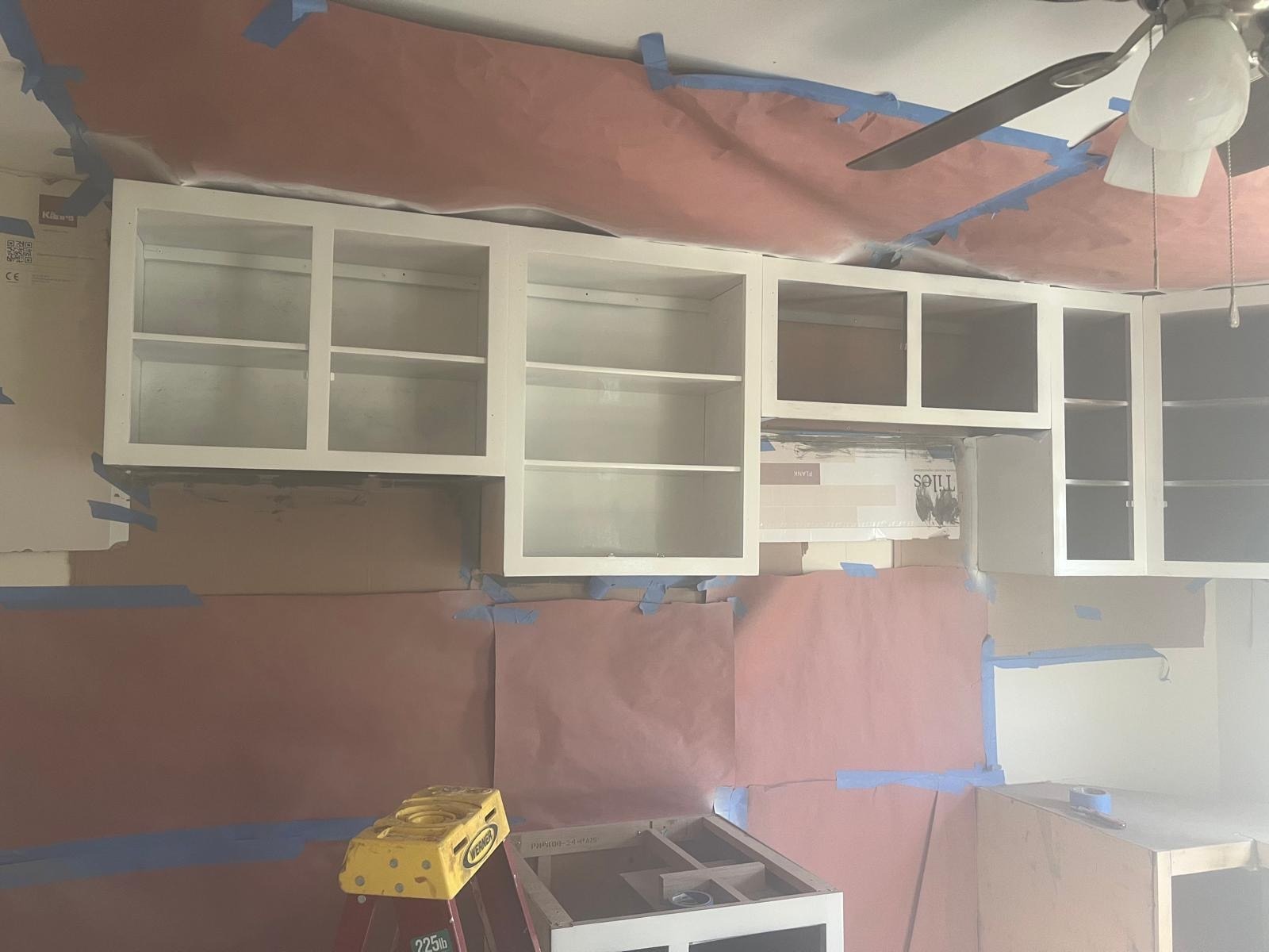 New white kitchen cabinets installed with walls and ceiling masked for paint